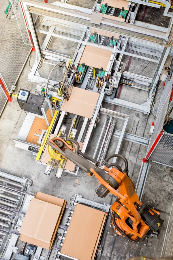 Vue en plongée d'un robot industriel automatisé manipulant des panneaux sur une chaîne de production dans l'usine Alsapan.