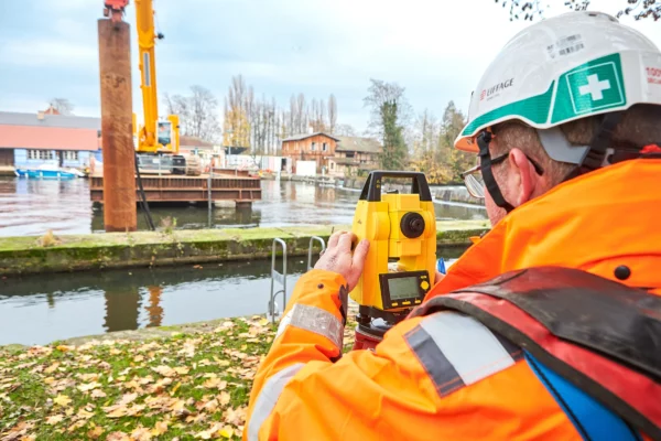 Géomètre réalisant un relevé topographique au théodolite sur un chantier VNF à Strasbourg dans le cadre d'un reportage photo de suivi de chantier.