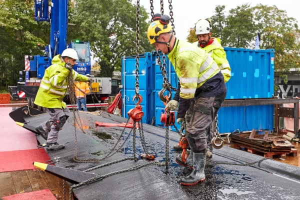 Équipe d'ouvriers réalisant la manutention d'un clapet à l'aide de chaînes et d'appareils de levage sur un chantier VNF à Strasbourg dans le cadre d'un suivi de chantier.