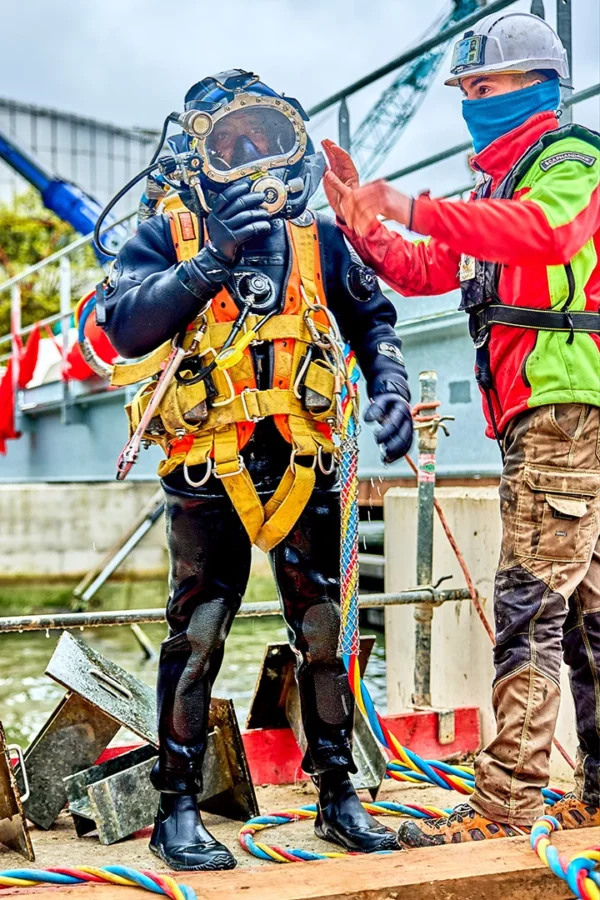 Scaphandrier professionnel équipé d'un casque de plongée assisté par un technicien lors d'une intervention sur le chantier VNF du barrage de la Robertsau à Strasbourg.