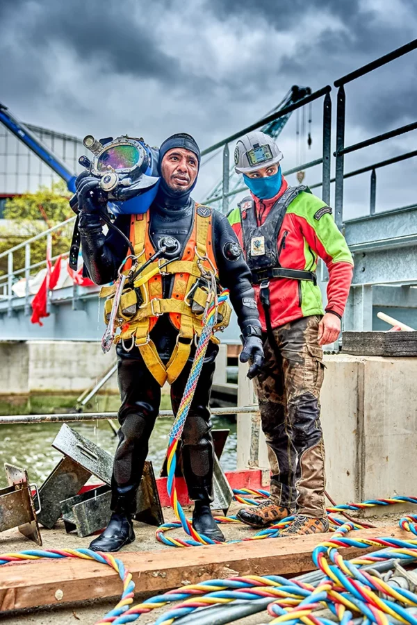 Scaphandrier professionnel équipé d'un casque de plongée assisté par un technicien lors d'une intervention sur le chantier VNF du barrage de la Robertsau à Strasbourg.